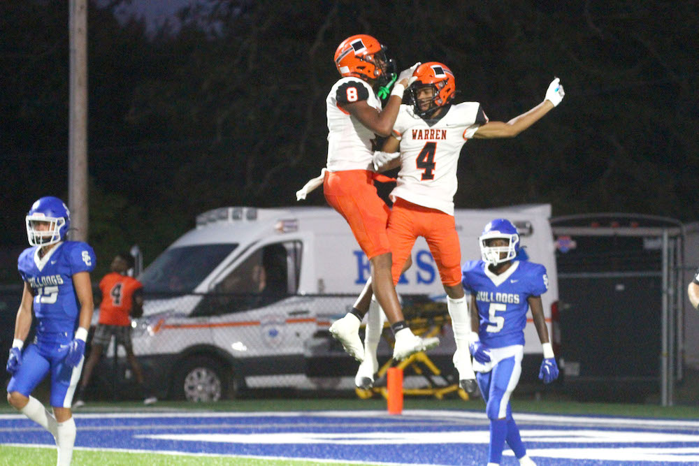Two football players jumping in the air to catch a ball.