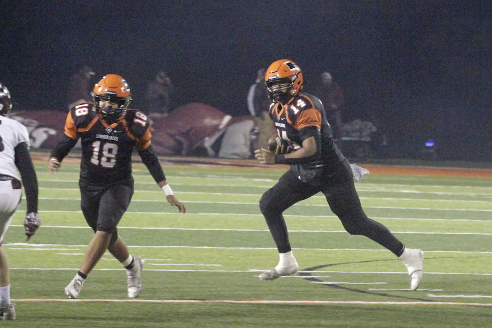 Two football players are running on a field.