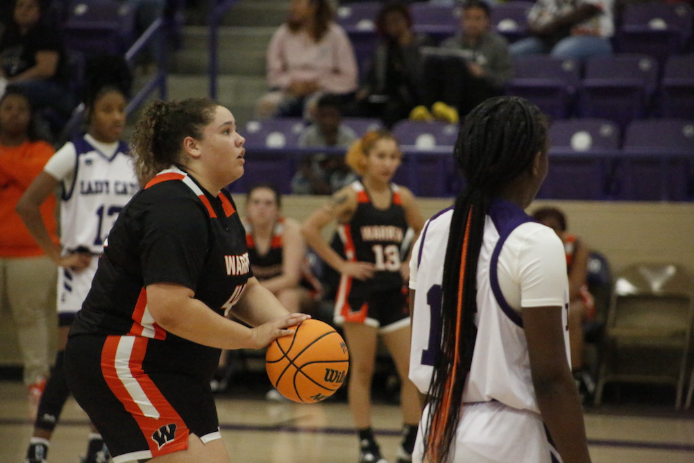 A girl in black and orange jersey holding a basketball.