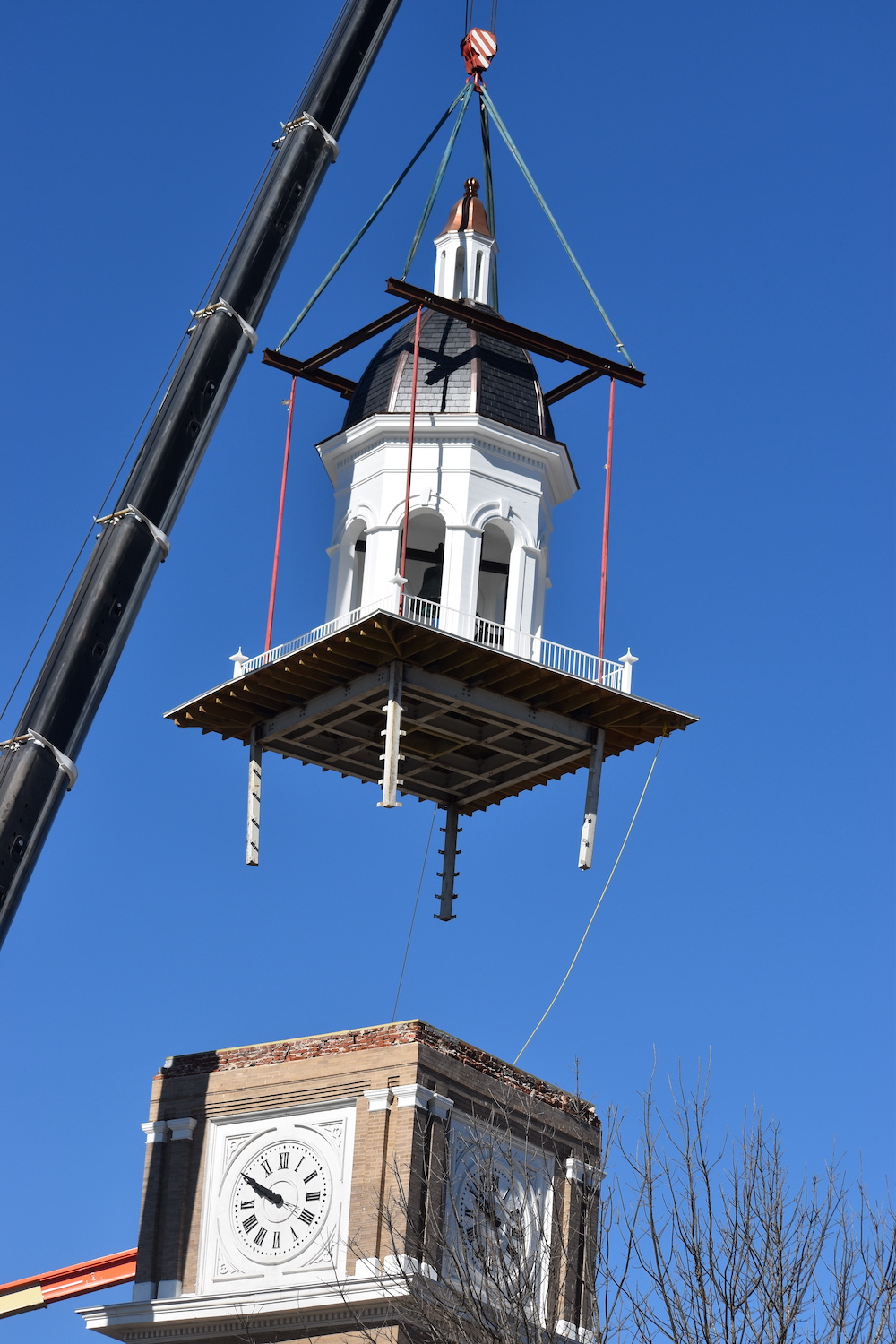 A crane is lifting a building with a clock tower.