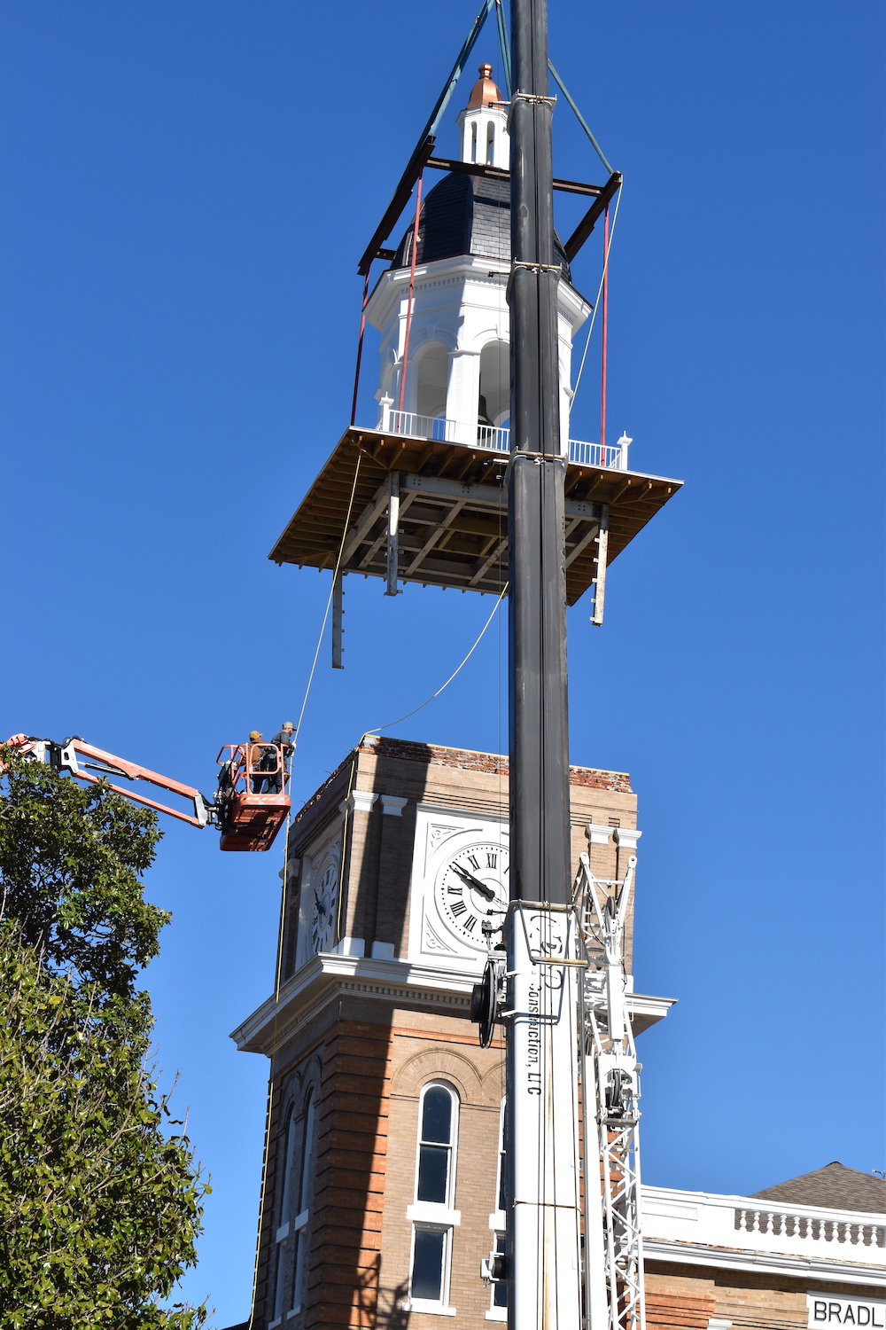 A man is hanging from the side of a clock tower.
