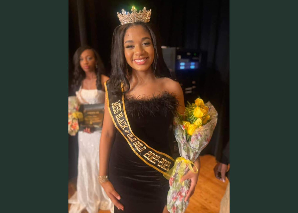 A woman in a black dress holding flowers and wearing a tiara.