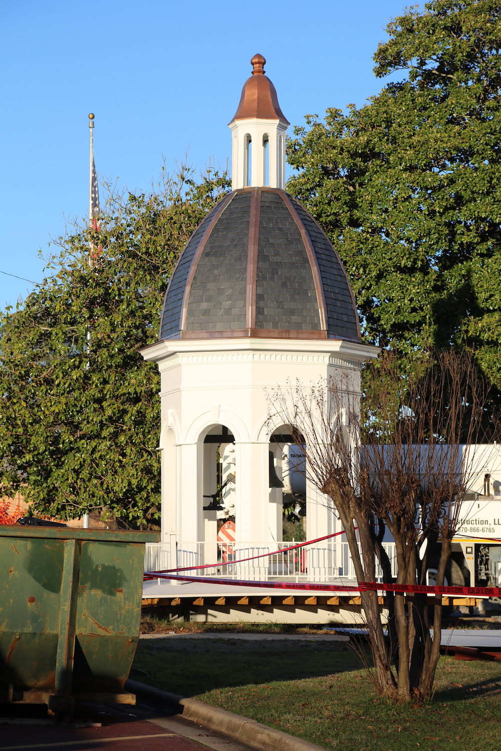 A white building with a dome top and a tree in the background.