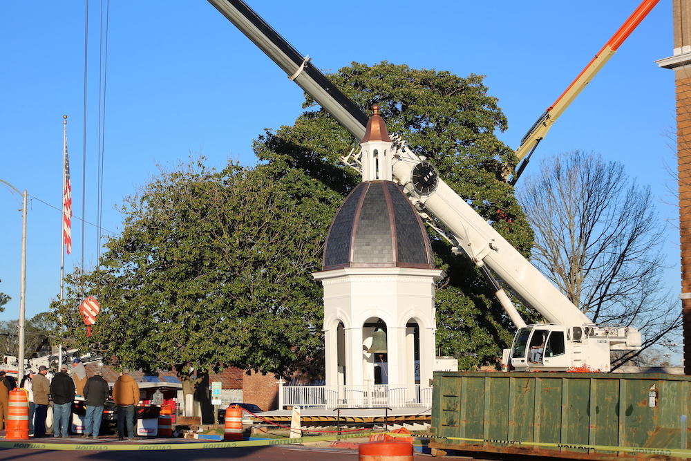 A crane is lifting up the top of a building.