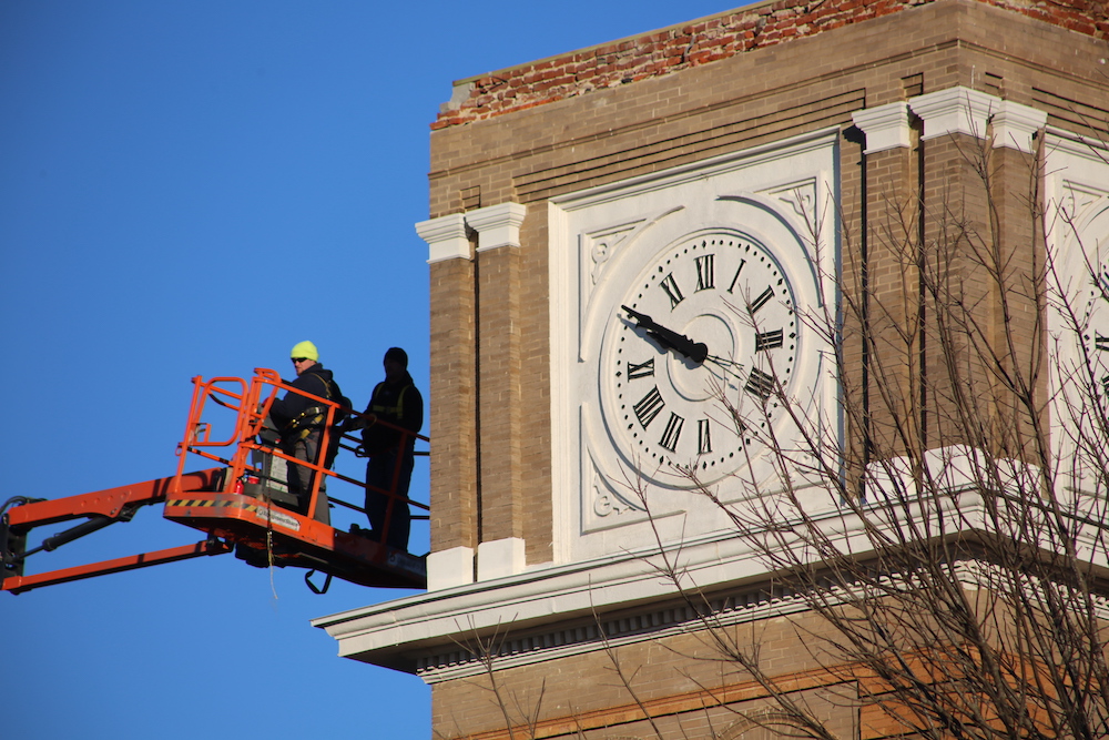 A man on a cherry-picker is standing next to a clock.
