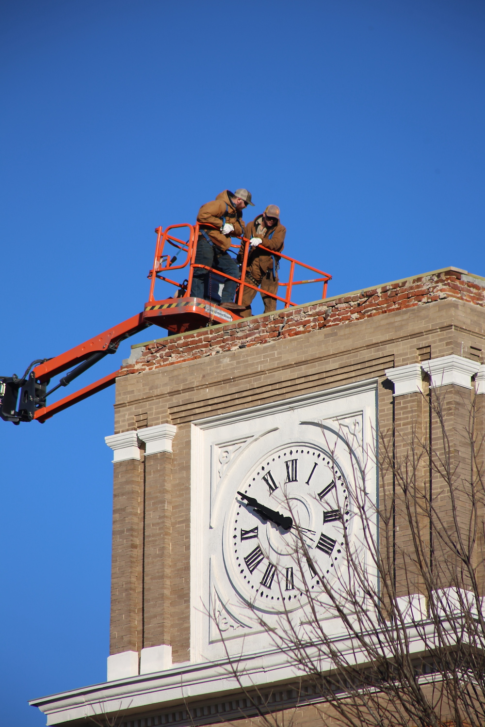 Two men in a cherry-picker working on the clock tower.