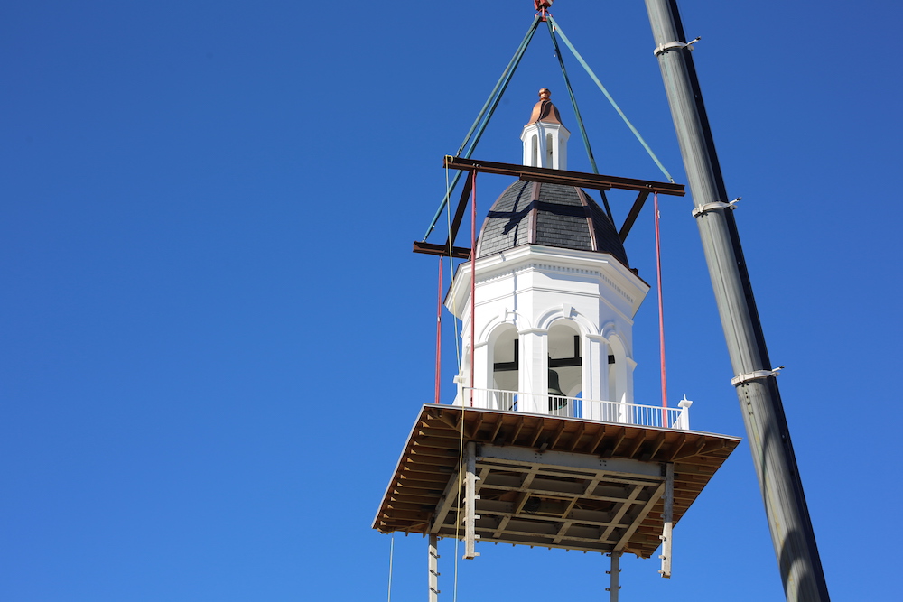 A crane is lifting a building with a clock tower.