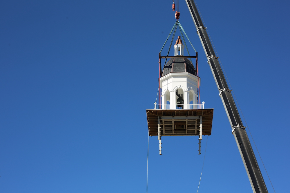 A crane is lifting a light house into the sky.