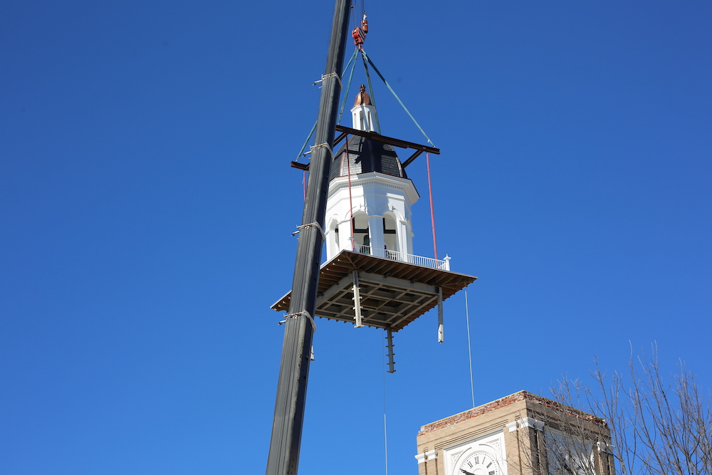 A large white clock tower is being lifted by crane.