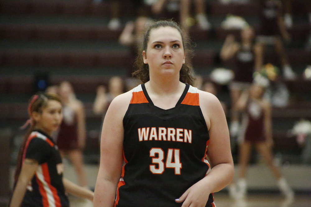 A woman in black and orange jersey holding basketball.