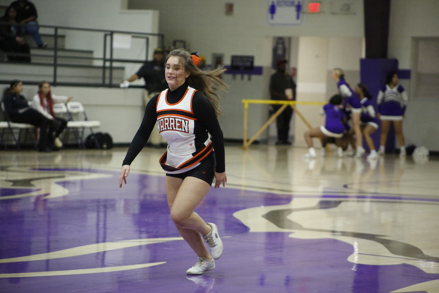 A girl in cheerleader uniform running on the court.