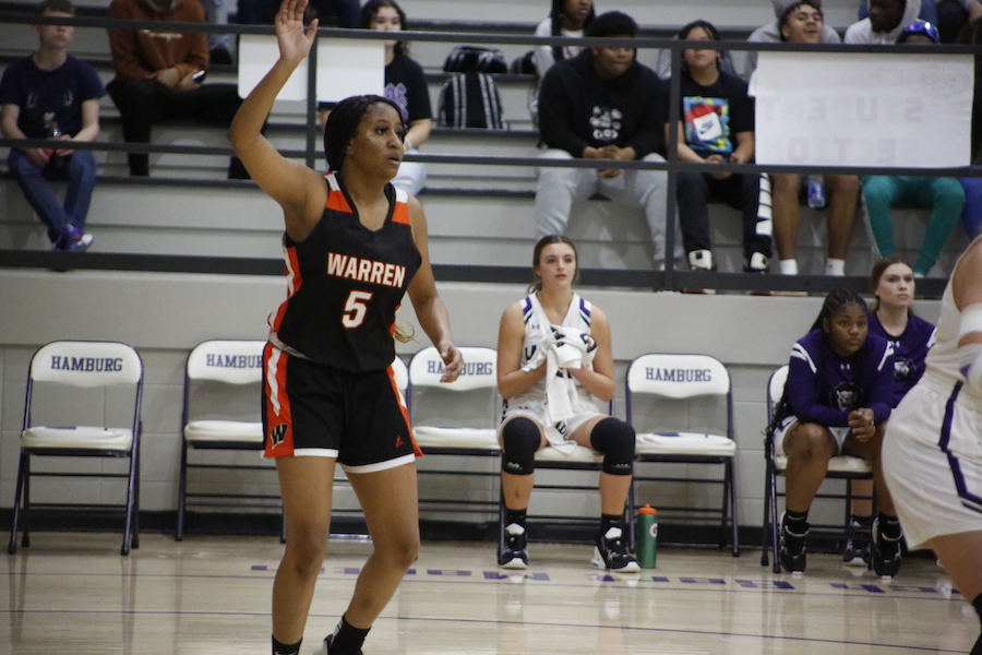 A woman in black and orange basketball uniform playing basketball.