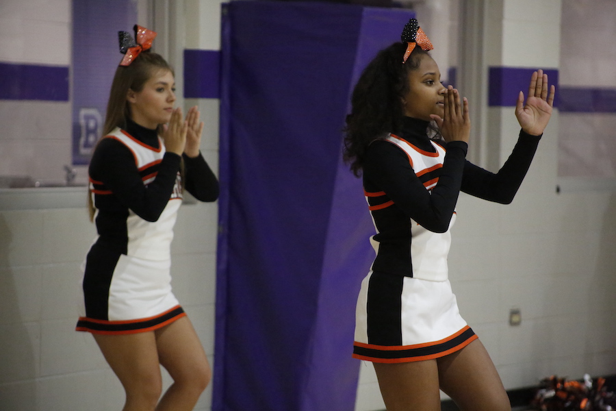 Two cheerleaders are standing in front of a mirror.