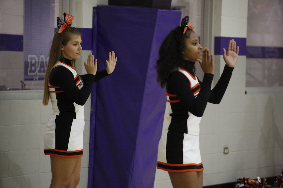 Two cheerleaders are standing in front of a purple wall.