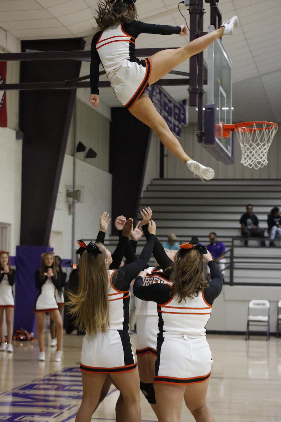 A cheerleader is in the air while holding onto a basketball hoop.