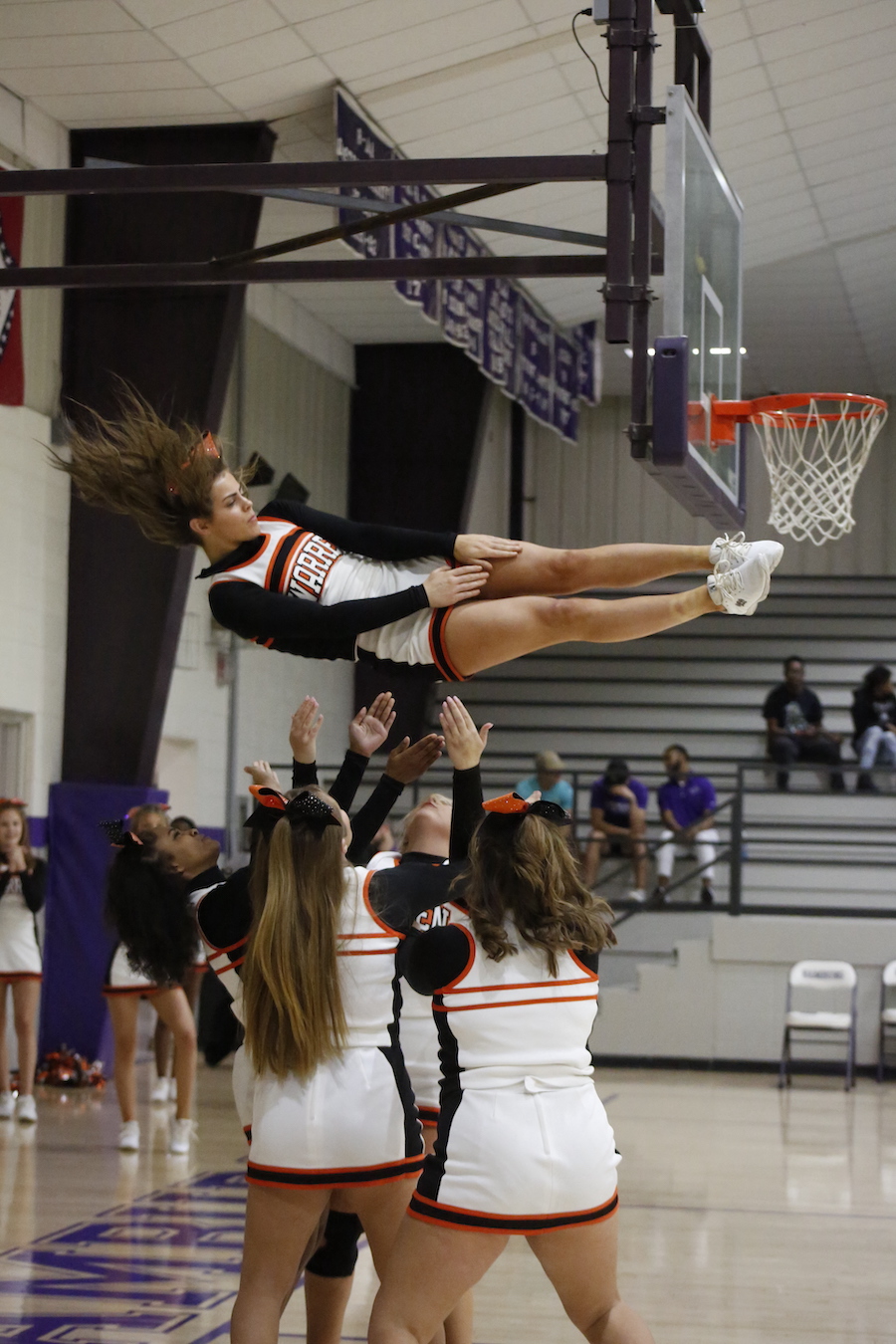 A cheerleader is in the air while holding onto a hoop.