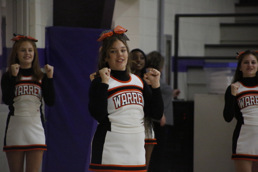 A girl in cheerleader uniform standing with her hands raised.
