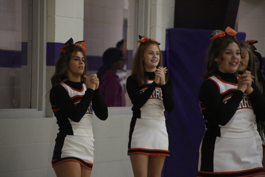 Three cheerleaders are standing in a row and one is clapping.