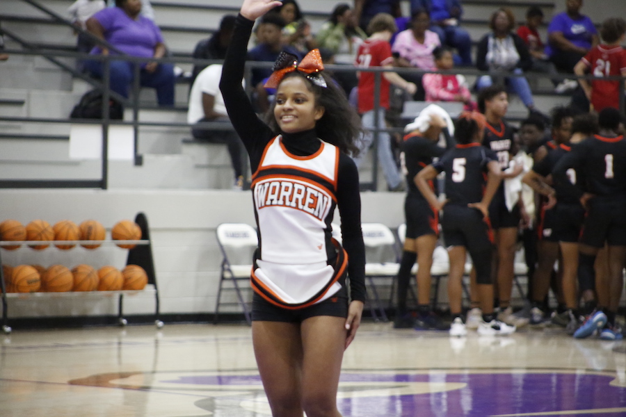A cheerleader waves to the crowd at a basketball game.
