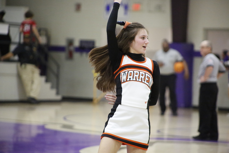 A girl in cheerleader uniform throwing her hand up.