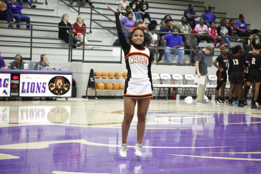 A cheerleader is standing on the court with her hands raised.