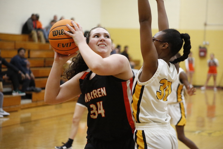 A woman holding onto the basketball while another person tries to block it.