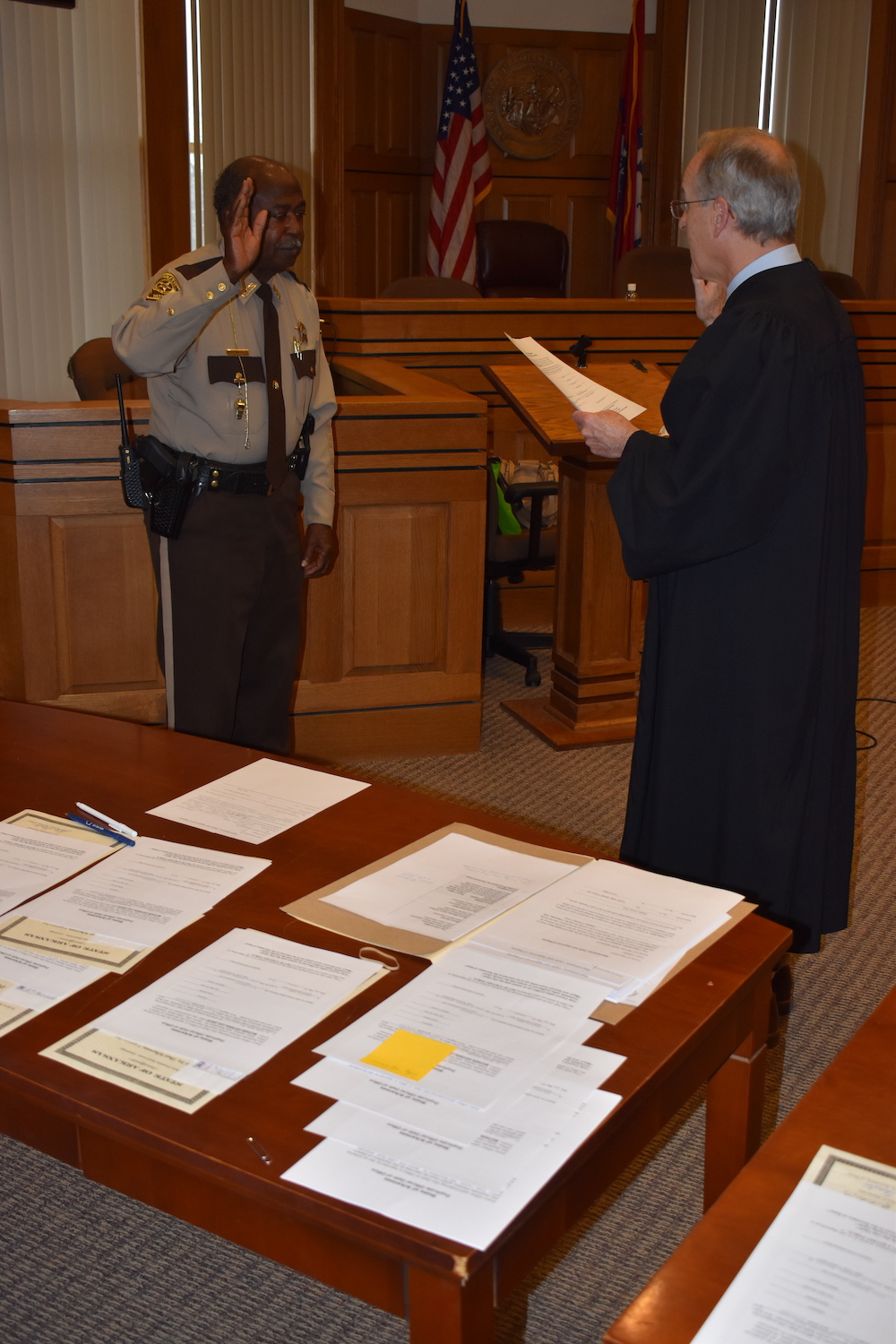 A judge and a police officer stand in front of papers.