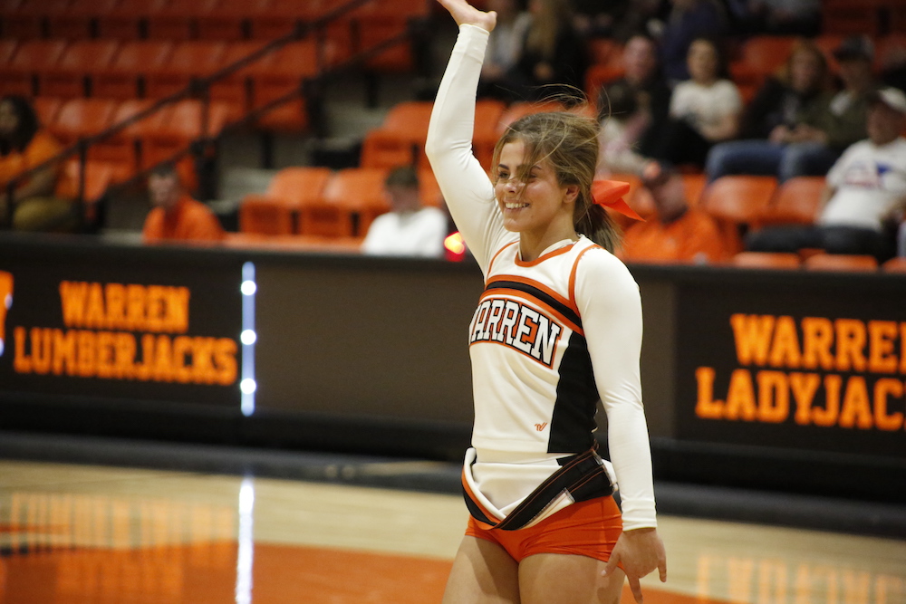A man in an orange jacket standing next to a tree.