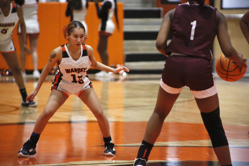 A girl in white and orange jersey playing basketball.