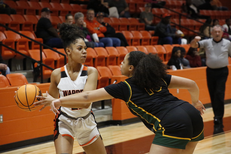 Two women playing basketball on a court with people watching.