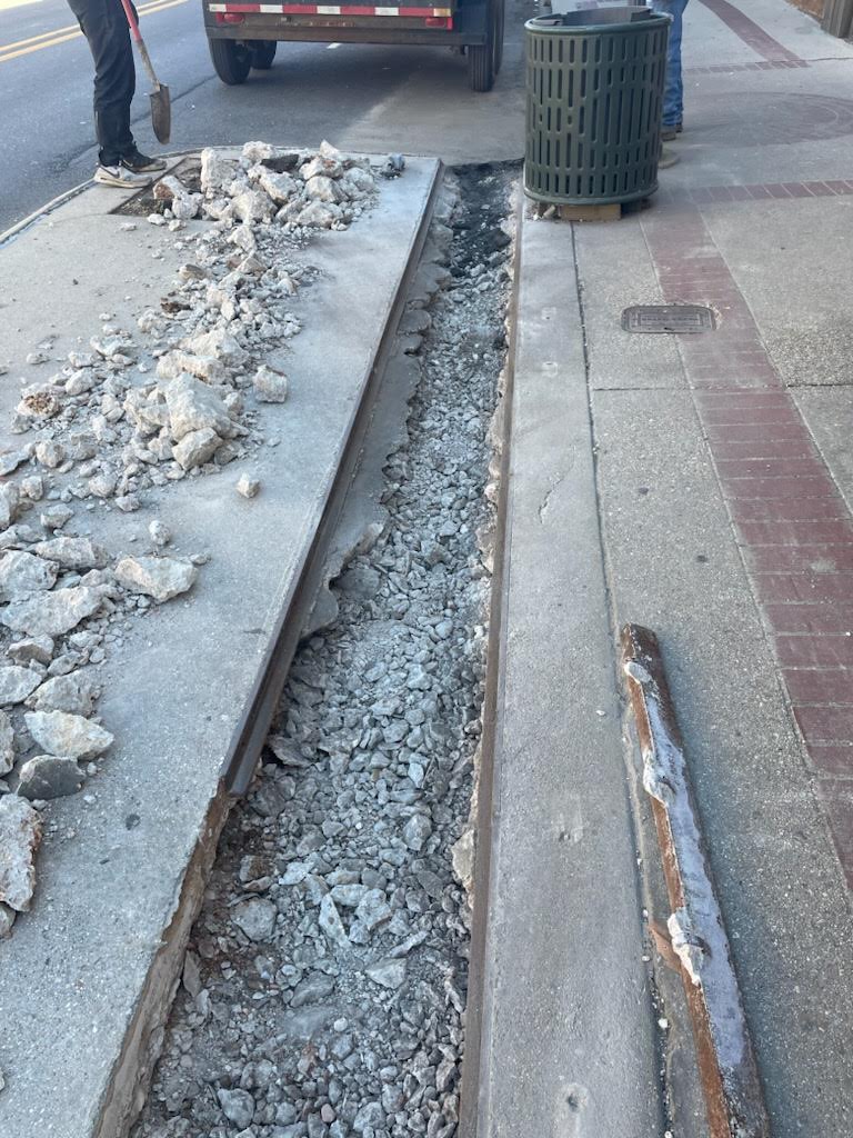 A street with broken concrete and a metal pole.