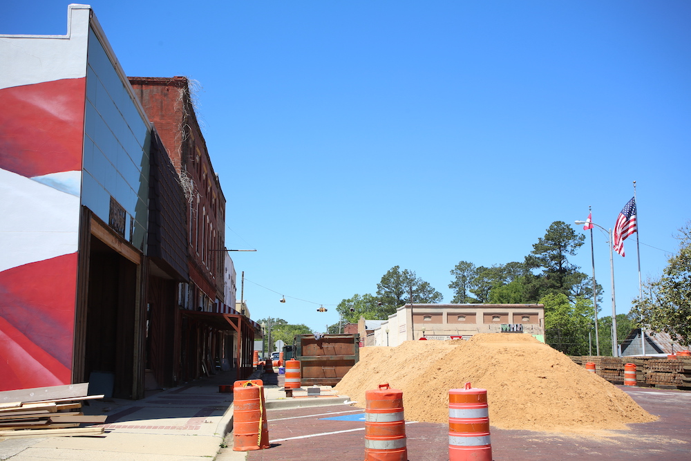 A street with orange cones and dirt on the side.