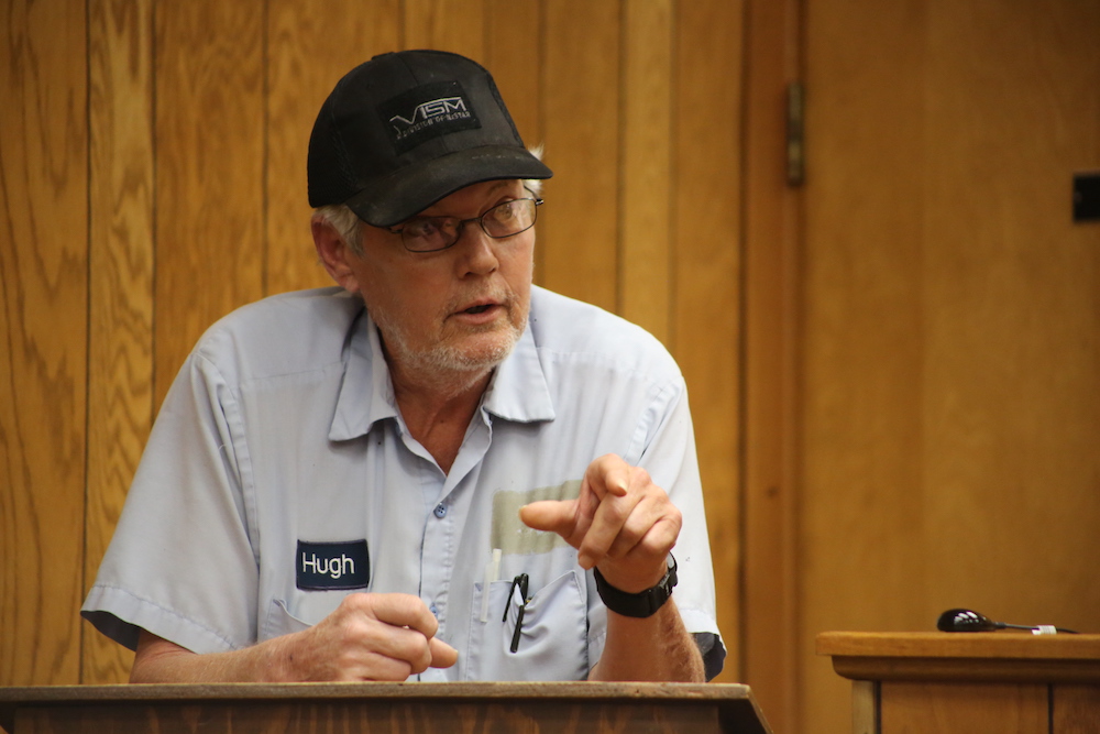 A man wearing a hat and glasses talking to someone.
