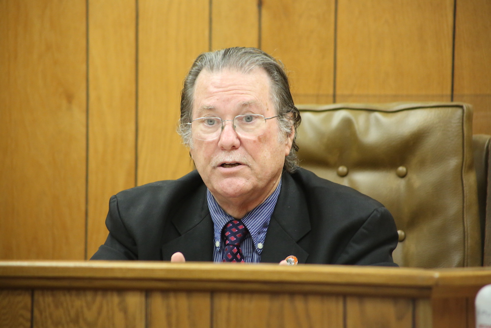 A man in suit and tie sitting at the front of a courtroom.
