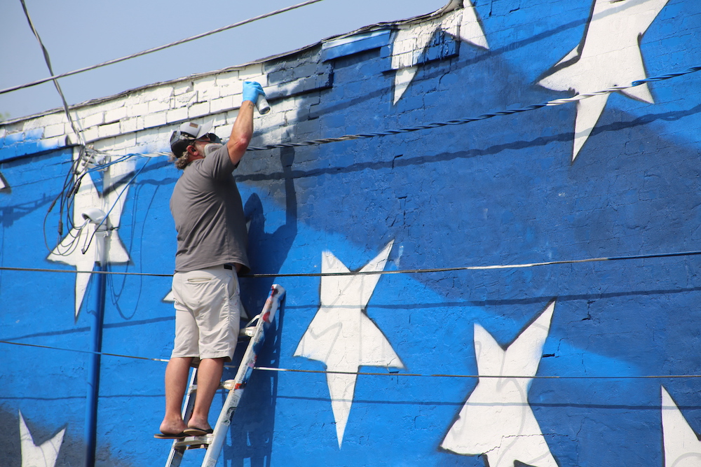 A man on a ladder painting stars on the side of a building.
