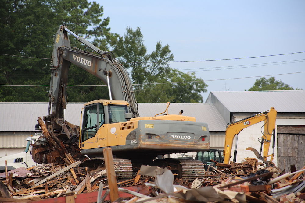A yellow and black excavator some trees and buildings