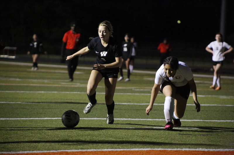 Two girls are playing soccer on a field.