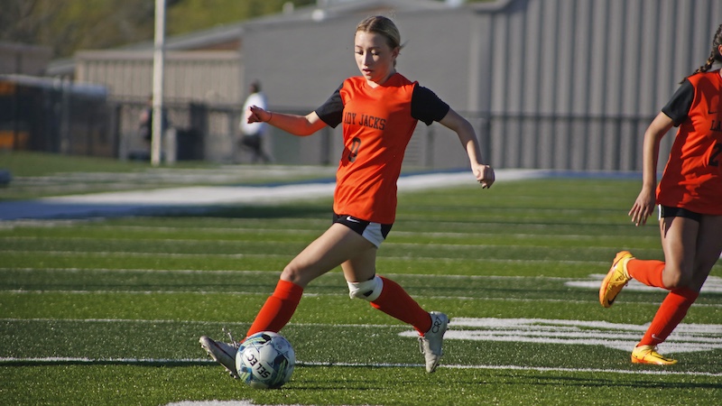 A girl in an orange shirt is kicking a soccer ball.