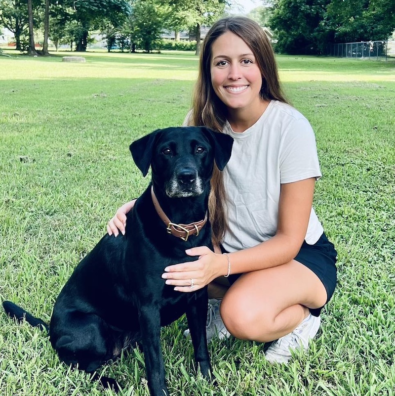 A woman kneeling down next to her black dog.