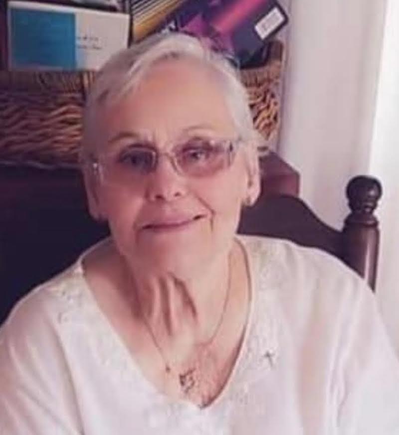 A woman with glasses sitting in front of a wall.