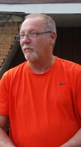 A man in an orange shirt is standing outside.