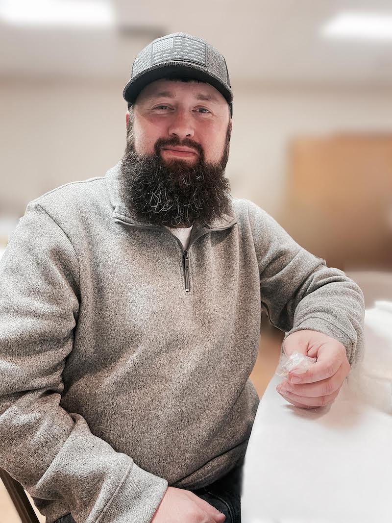 A man with a beard and hat sitting in front of papers.