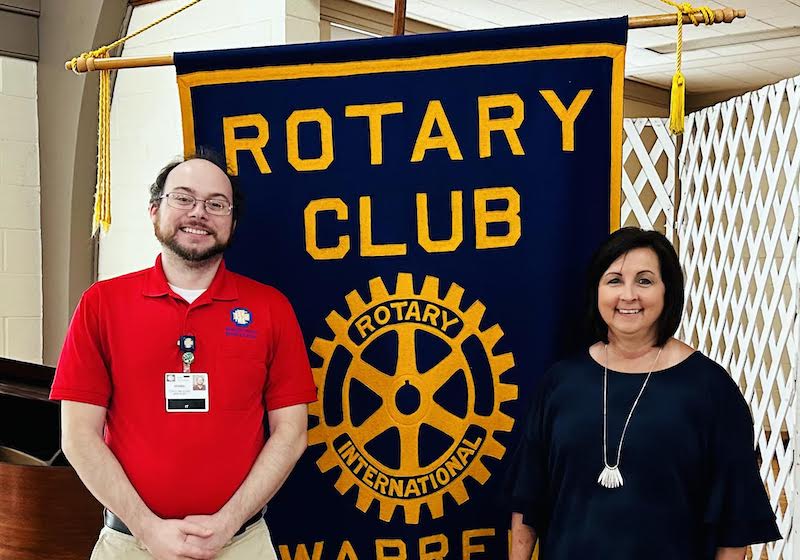 Two people standing next to a rotary club banner.