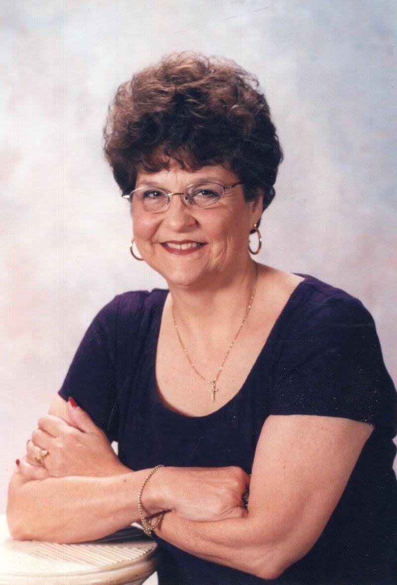 A woman with glasses and a necklace is smiling.