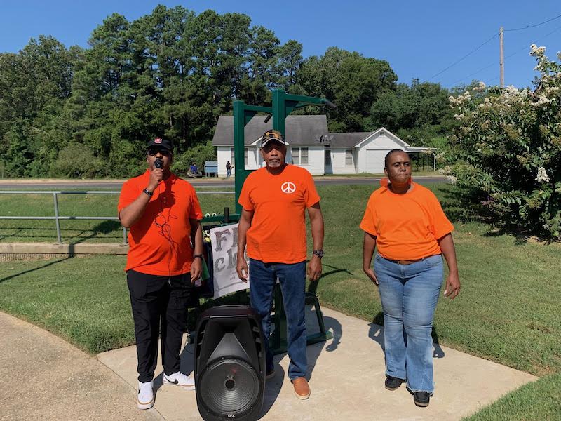 Three people standing next to a cart in the grass.