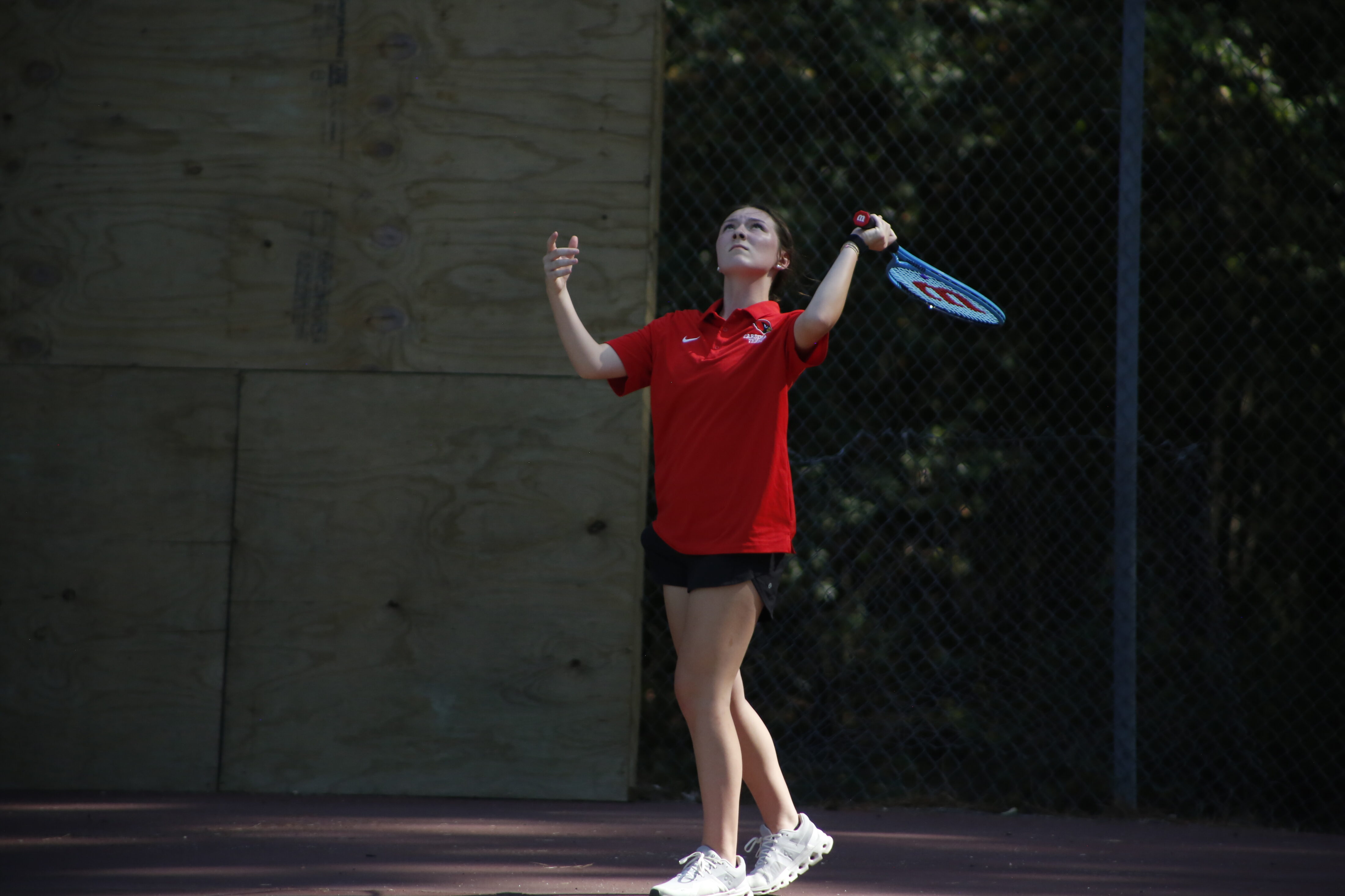 A woman in red shirt and black shorts playing tennis.