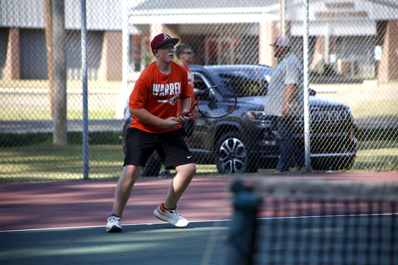 A man in an orange shirt playing tennis.