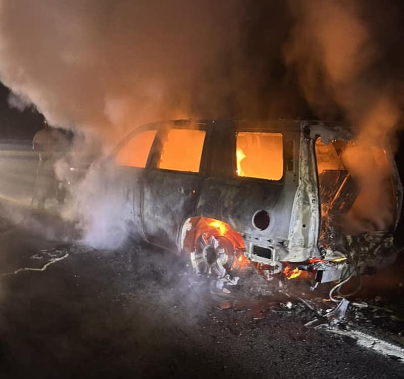 A van is burning on the side of the road.