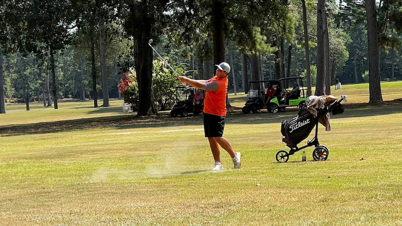 A man swinging at a golf ball on the green.