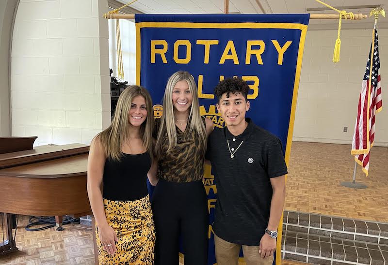 Three people standing in front of a rotary club banner.